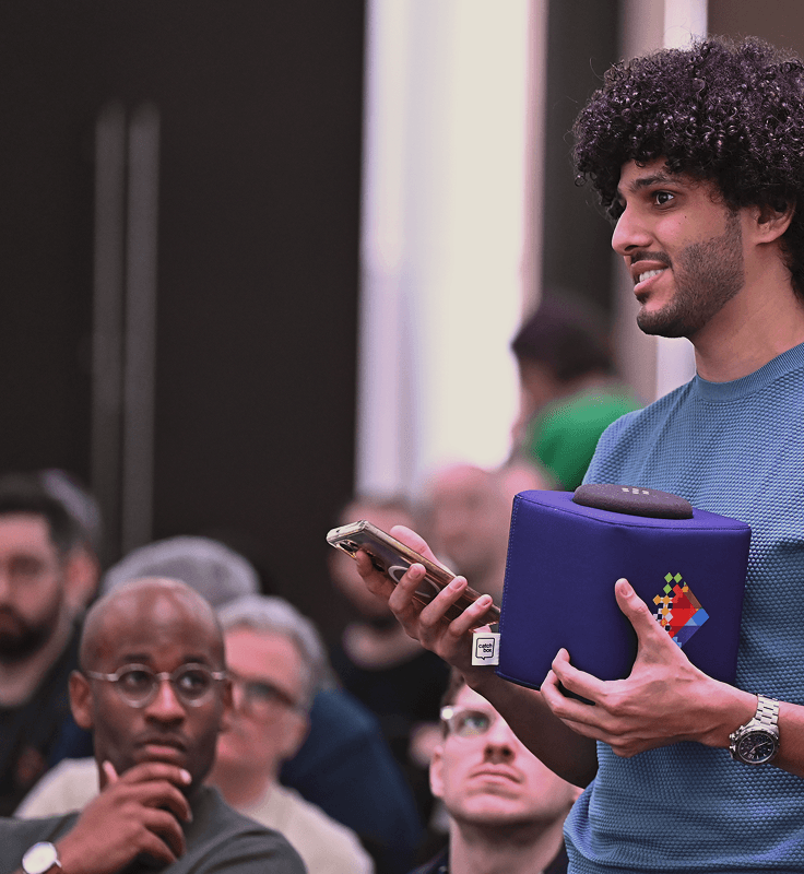 In a bustling Dubai event, a man in a blue shirt actively participates during question time by holding a microphone amidst a diverse audience.